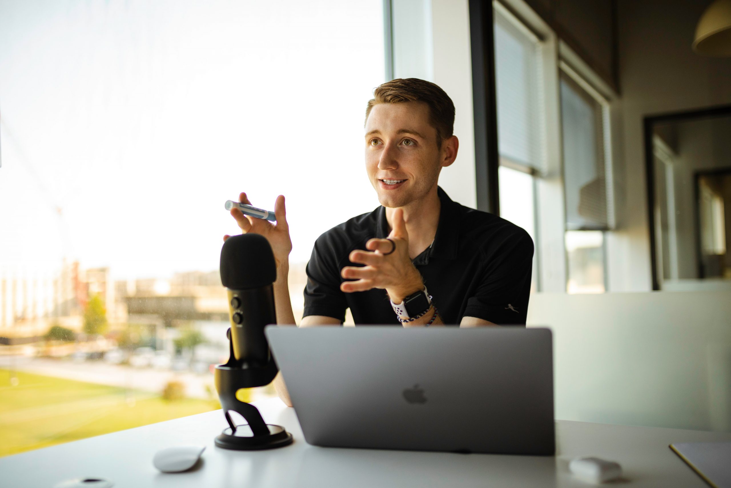 A man sat at a laptop, with a large microphone creating a podcast.